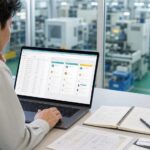 工場を背景に営業リストとCRM画面を確認する製造業の担当者